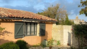 A rustic house with a tiled roof, a stone wall, and a garden area with plants and a small pond.