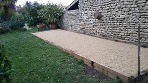 A garden with a gravel path, a wooden deck, and a stone wall.
