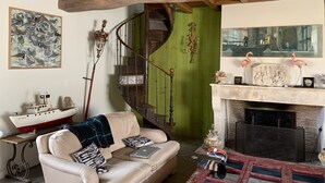 A cozy living room with a wooden ceiling, a green wall, a fireplace with decorative items, a staircase, and a large abstract painting.