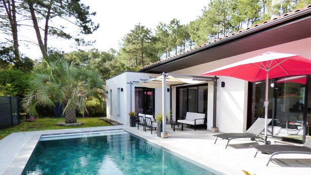 A modern outdoor pool area with a clear pool, lounge chairs, and a covered seating area with a red umbrella.