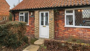A two-story house with a red-tiled roof, a white door, and a small garden area with bushes and a pathway. - Cornerways, 8 North Lane (York)