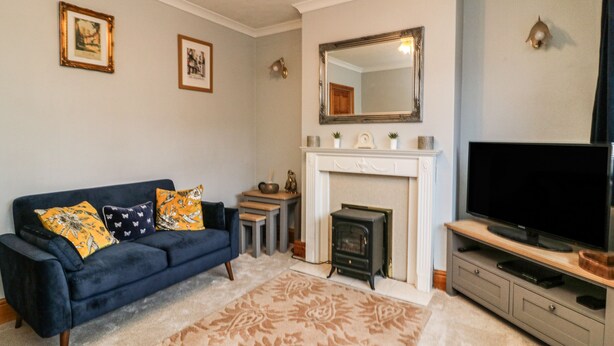 A living room with a blue sofa, a fireplace, a television, and framed pictures on the wall. - Cornerways, 8 North Lane (York)