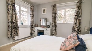 A bedroom with a bed, a dresser, a desk, and two windows with curtains. - Cornerways, 8 North Lane (York)