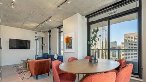 Een moderne vergaderruimte met een ronde tafel, rode stoelen met bekleding, een groot raam met uitzicht op de stad, een flatscreen televisie en een kleurrijk vloerkleed.