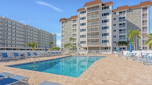 A swimming pool with lounge chairs and a stone-tiled deck, surrounded by multi-story buildings with balconies. - HELLO SUNSHINE! FUN IN THE SAND! FAMILY ISLAND VACATION ON A BUDGET! (Fort Myers Beach)