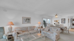 A living room with two sofas, a coffee table, lamps, a framed picture, and a dining area with chairs and a table. - HELLO SUNSHINE! FUN IN THE SAND! FAMILY ISLAND VACATION ON A BUDGET! (Fort Myers Beach)