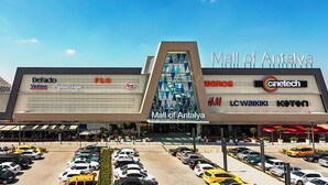 El exterior del Centro Comercial Mall of Antalya, con nombres de tiendas visibles como DeFacto, FLO, H&M, LC Waikiki y Koton.