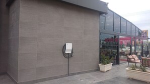 Fachada moderna de un edificio con pared de ladrillo gris, escaparate de vidrio y mesas al aire libre con plantas en macetas.