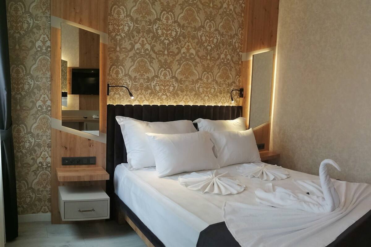 A hotel room with a bed, a TV, a wooden nightstand, and a mirror.