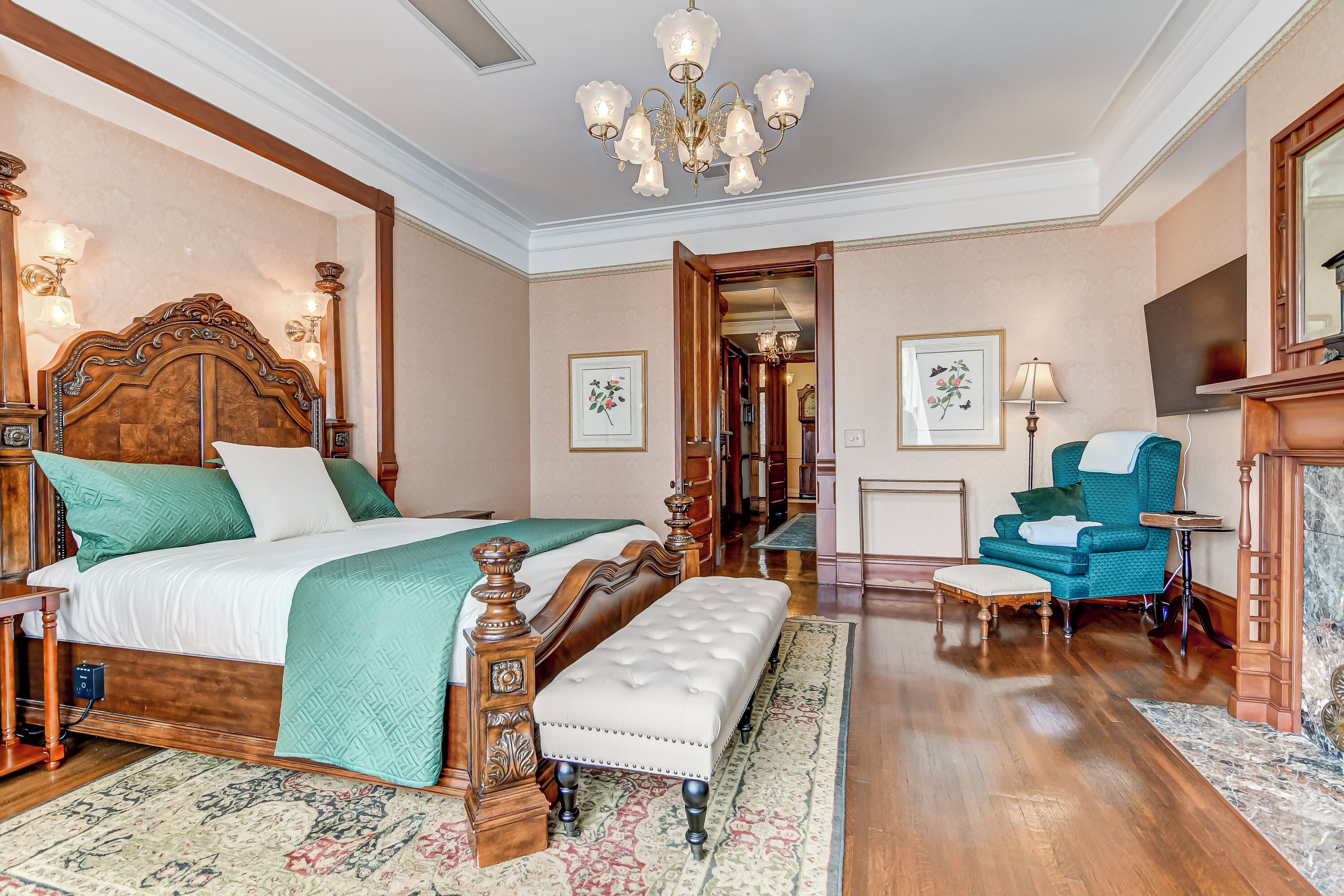 A spacious bedroom with a large bed, a wooden headboard, a bench, a blue armchair, and a chandelier.