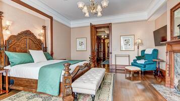 A spacious bedroom with a large bed, a wooden headboard, a bench, a blue armchair, and a chandelier.