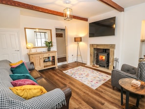 A cozy living room with a fireplace, wooden floors, a sofa with colorful cushions, a television, and a floor lamp.