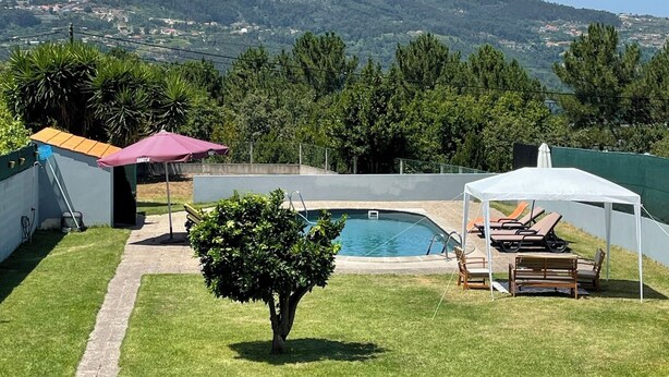 Ein Garten mit Swimmingpool, einer überdachten Sitzgelegenheit und Blick auf eine Hügelkette.