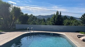 Ein klares Schwimmbecken mit Stufen, umgeben von einer gepflasterten Liegefläche und Blick auf eine hügelige Landschaft.