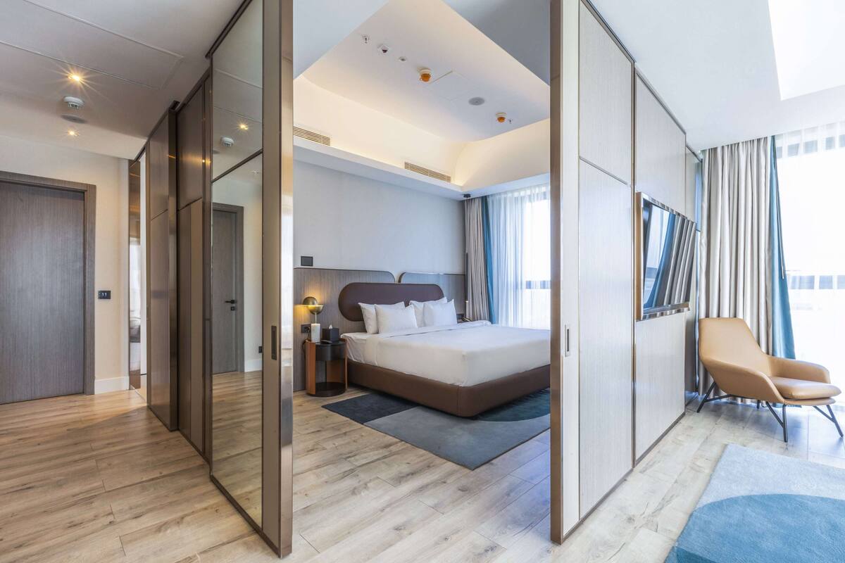 A modern hotel room with a large bed, a seating area, and a view of the city.