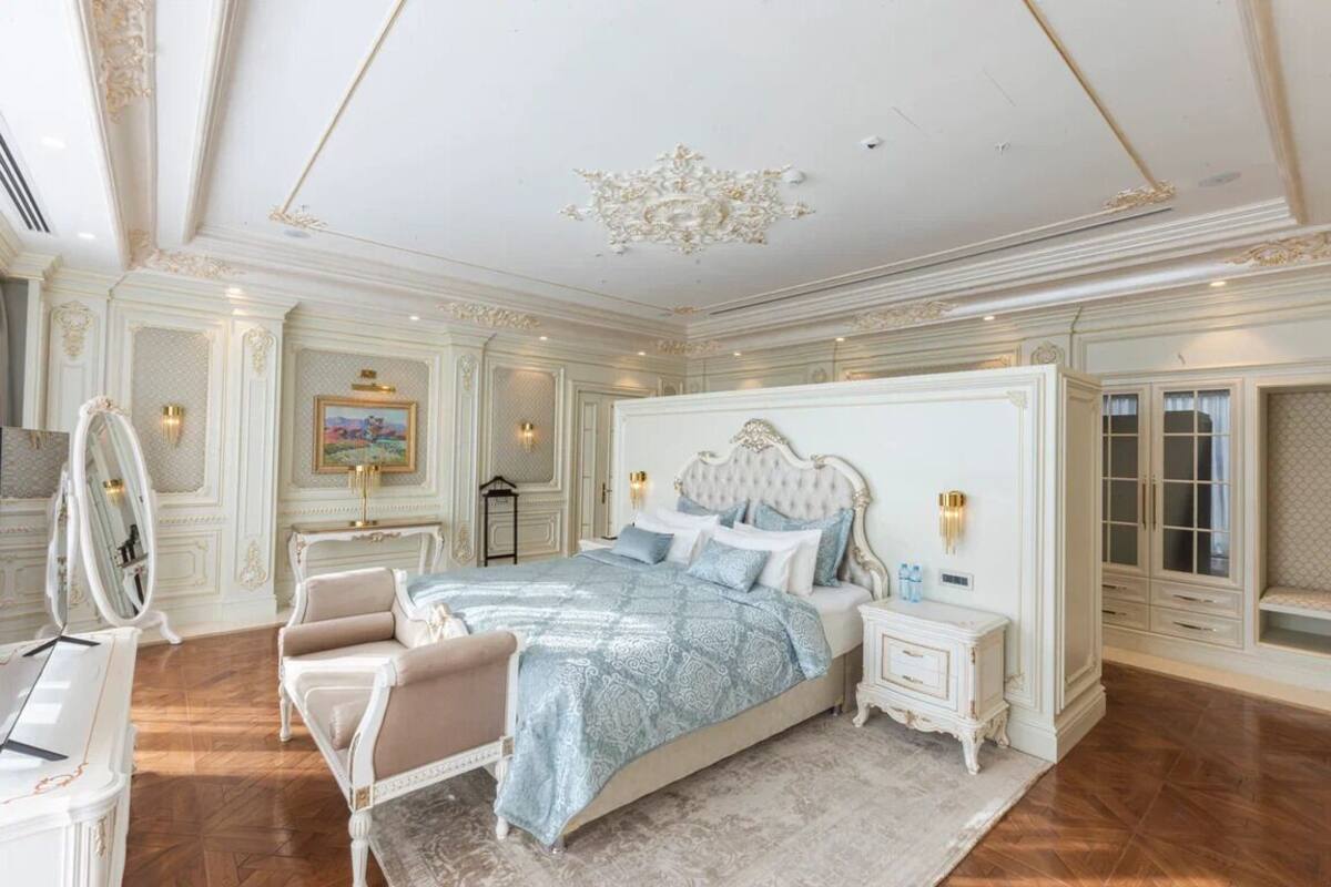 A luxurious bedroom with a large bed, a vanity with a mirror, and a dresser.
