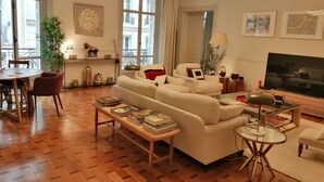 A modern living room with a sofa, a coffee table, a TV, and a dining area with a table and chairs. - Etoile-Champs Elysée (Paris)
