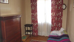 A bedroom with a wooden dresser, a small table, a bed with a colorful blanket, and floral curtains. - Villa in the center of Crozon (Crozon)