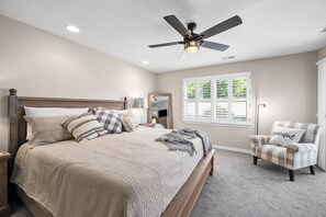 A bedroom with a bed, a ceiling fan, a window with blinds, and a chair.