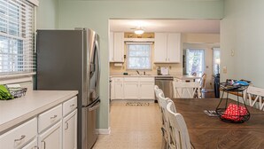 A compact kitchen with white cabinets, a stainless steel refrigerator, and a dining area with a wooden table and chairs.