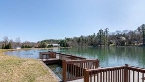 A lakeside wooden dock with a grassy area and a building in the background.