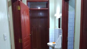 A narrow hallway with wooden flooring, a red door on the left, a white sink with a mirror above it, and a blue tiled wall. - Stay.Plus Naivasha Budget Apartment (Naivasha)