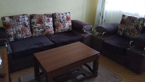 A living room with a dark-colored sofa set, a wooden coffee table, and patterned throw pillows. - Stay.Plus Naivasha Budget Apartment (Naivasha)