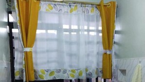 A small kitchen with a sink, a pink basin, and a window with yellow curtains. - Stay.Plus Naivasha Budget Apartment (Naivasha)