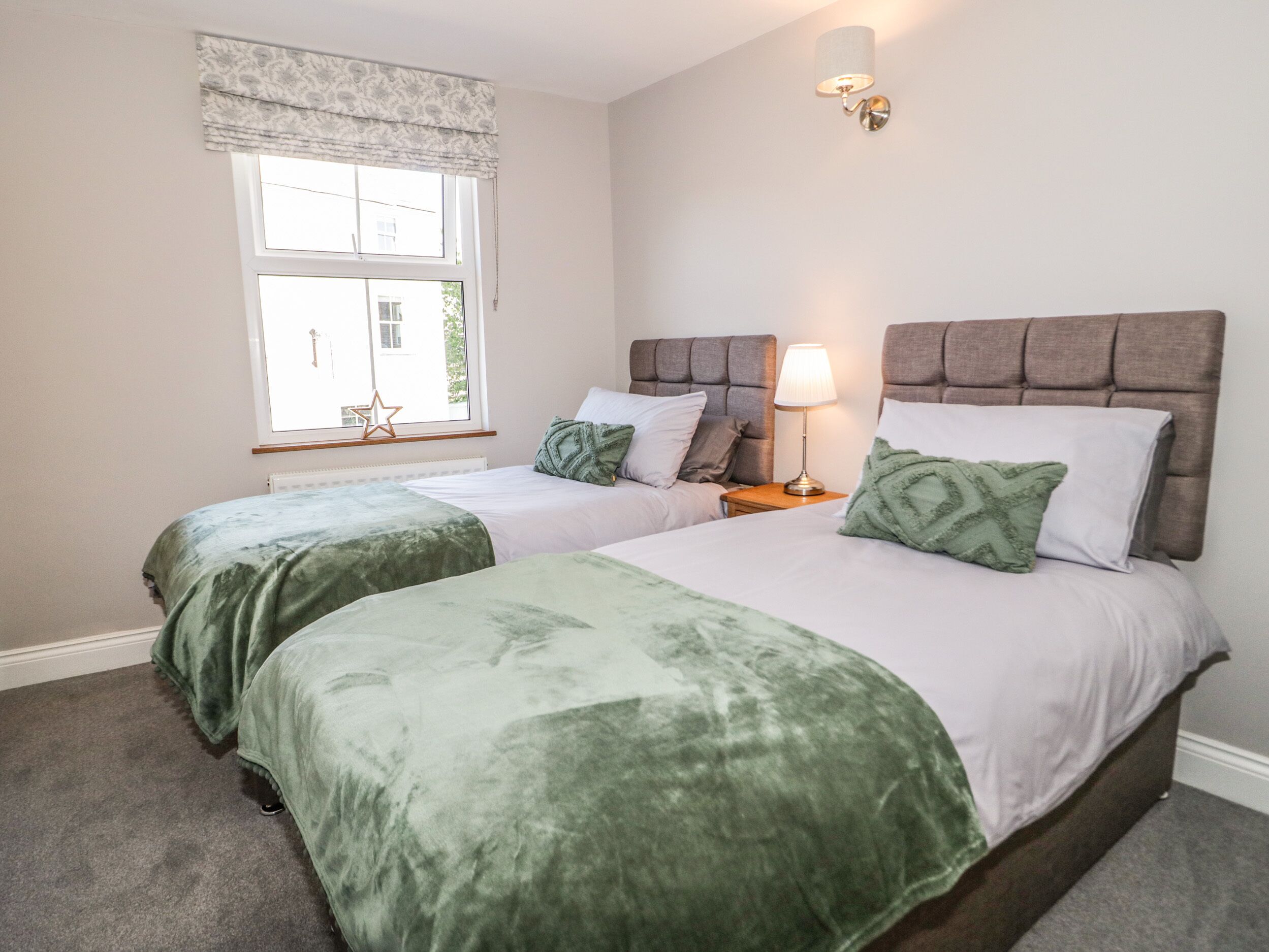 A bedroom with two beds, a window with a curtain, a wall-mounted lamp, and a star decoration.