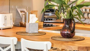Una cocina con una mesa de madera, dos sillas blancas, un florero con plantas verdes y una caja de pañuelos.