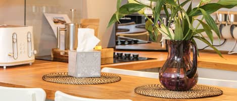 A kitchen with a wooden table, two white chairs, a vase with green plants, and a tissue box.