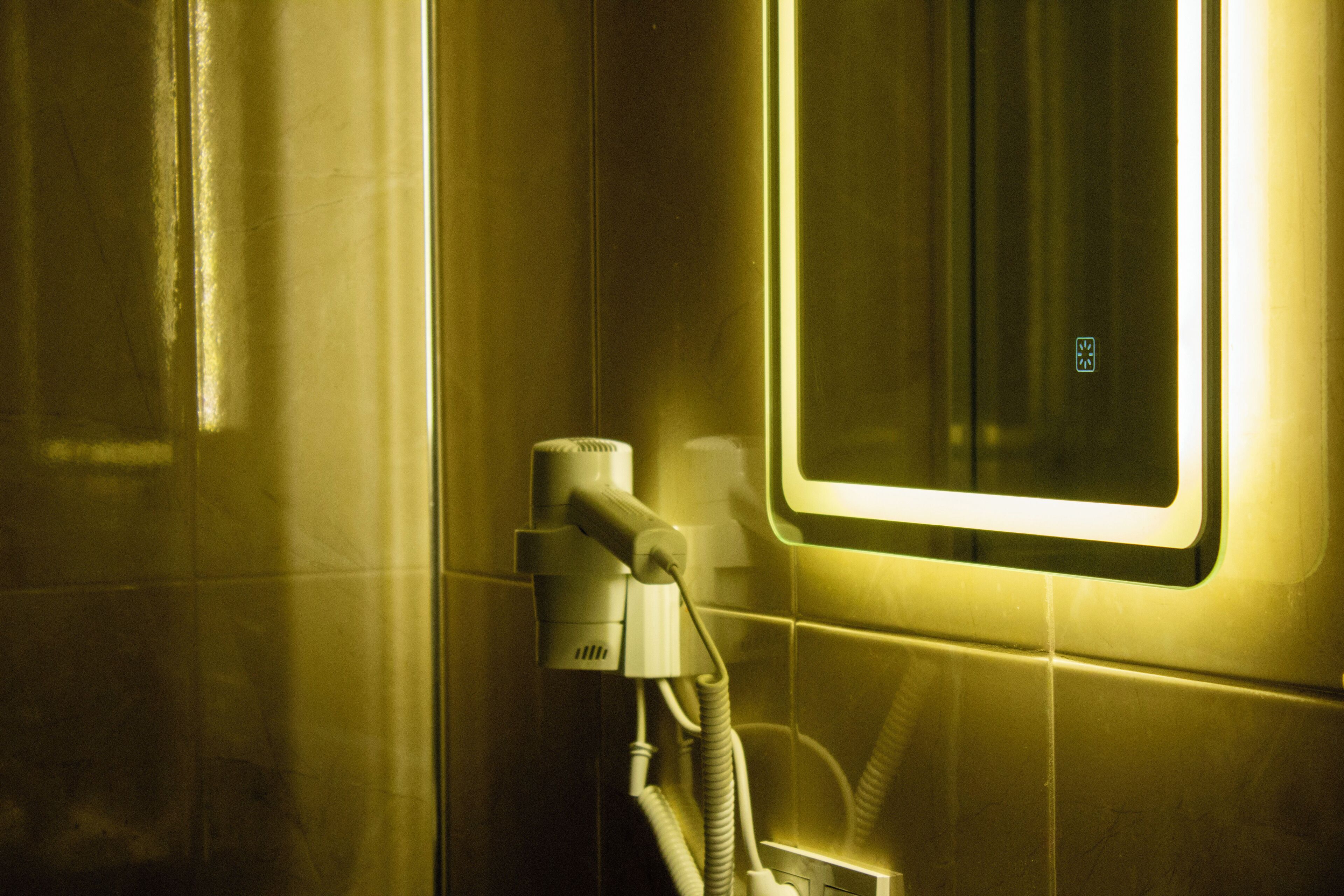 A bathroom with a hand dryer, a mirror, and a tiled wall.