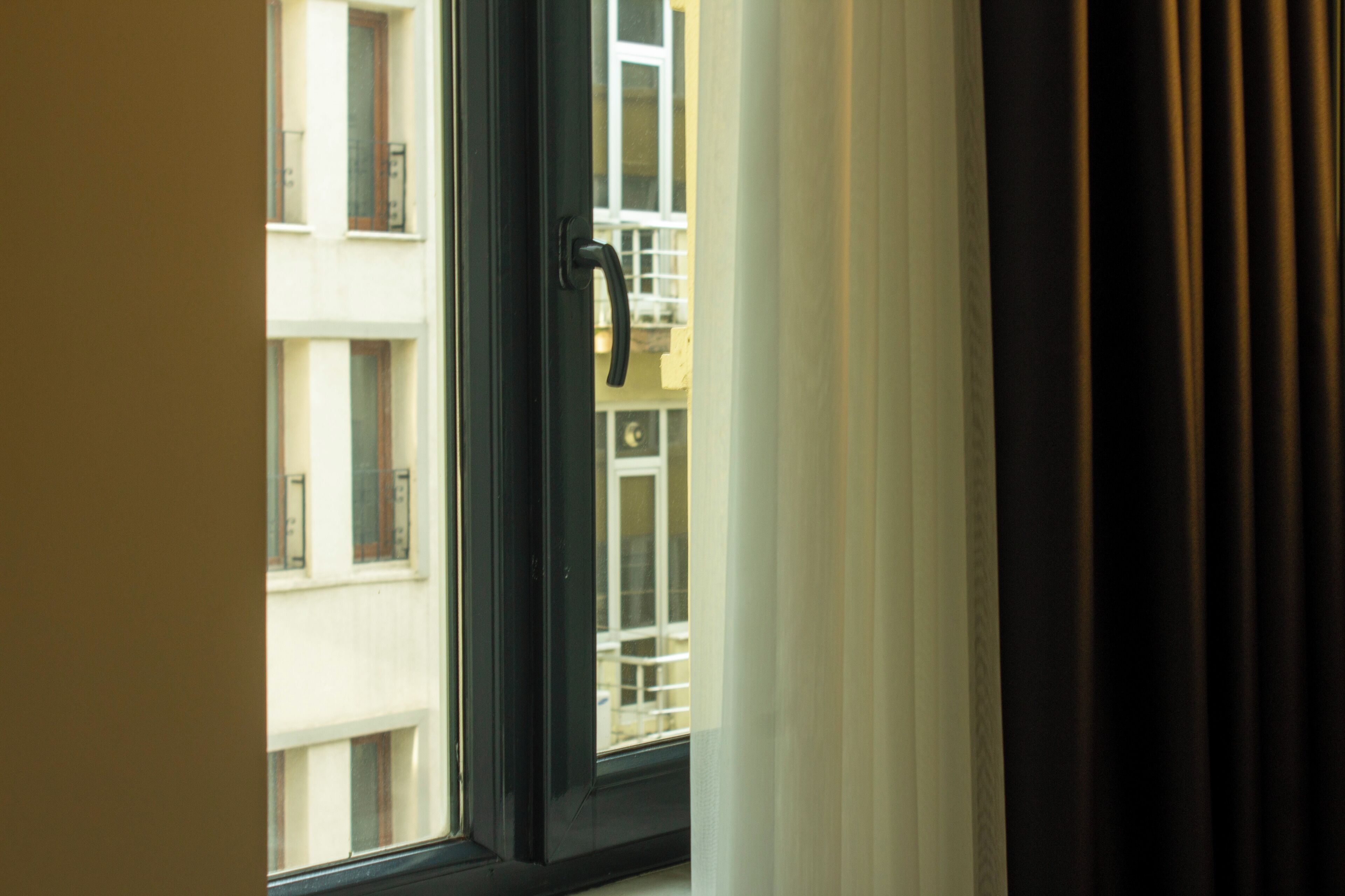 A window with a black frame and a white curtain partially drawn to the side.