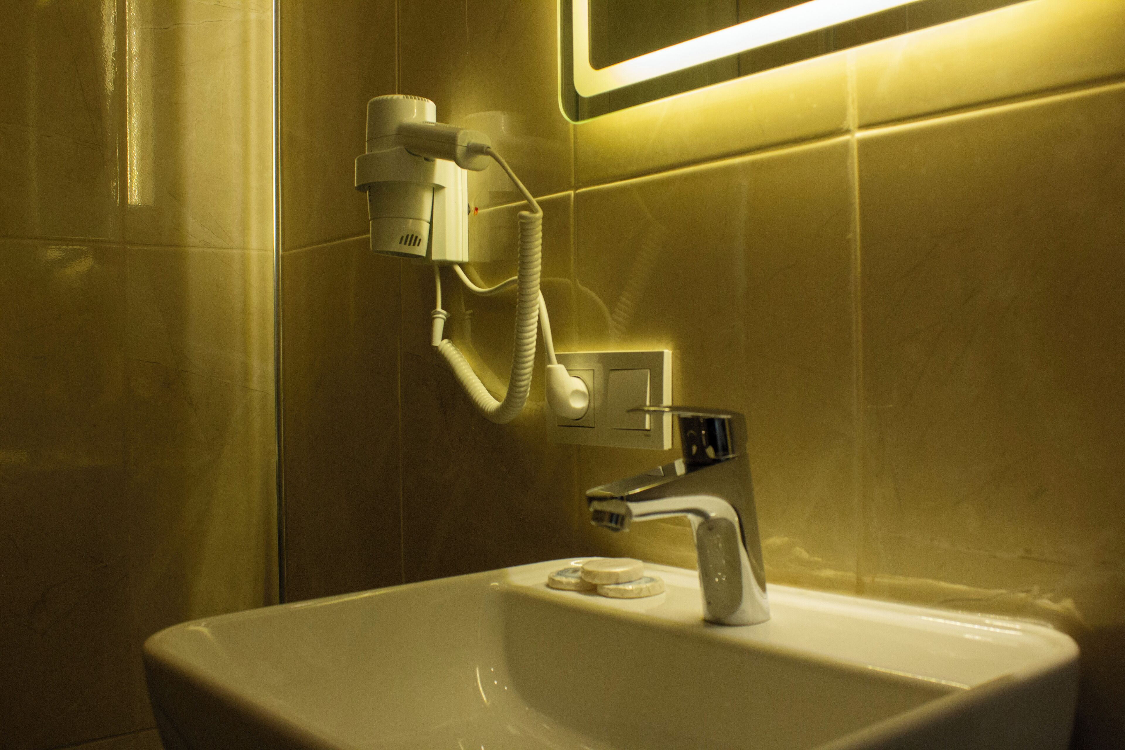 A bathroom with a white sink, a mirror, and a hairdryer mounted on the wall.