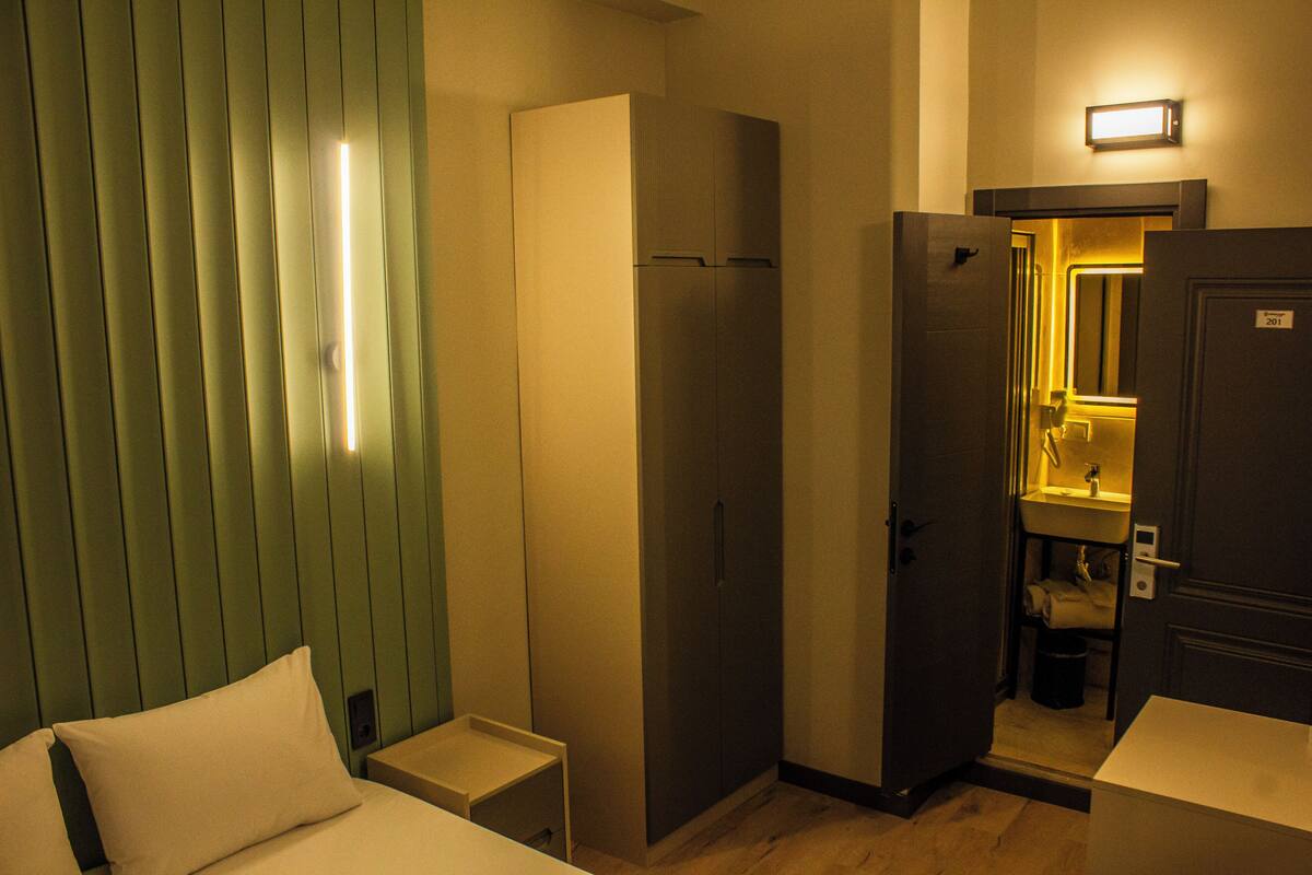 Une chambre d’hôtel avec un lit, une armoire, une salle de bain avec un lavabo et un miroir, et une petite table.