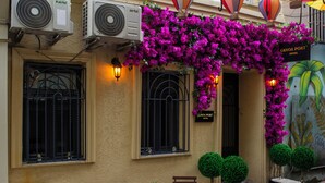 A hotel entrance with air conditioning units, a sign reading "GENOA PORT HOTEL," and a vibrant purple flower wall. - Genoa Port Hotel (Istanbul)