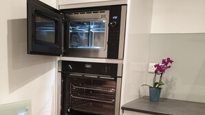 A compact kitchen with two ovens, a built-in microwave, and a small potted orchid on the counter. - Stylish detached studio with a wet room, Satellite TV & other amenities 😀 (Bristol)