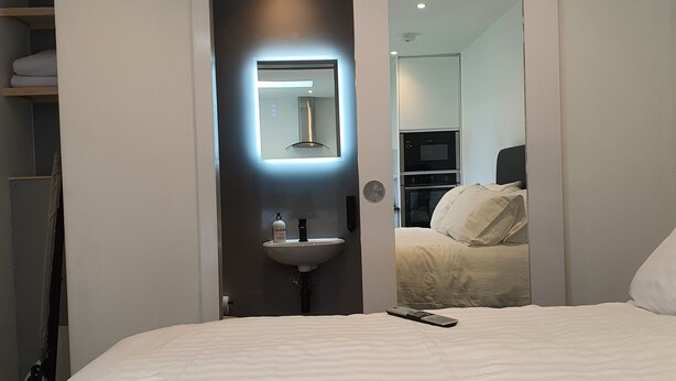 A hotel room with a large bed, a bedside table, a mirror, a built-in sink, and a wardrobe. - Stylish detached studio with a wet room, Satellite TV & other amenities 😀 (Bristol)