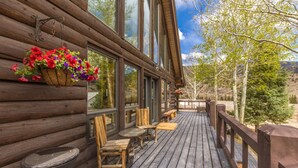 A wooden cabin with a porch, a wicker chair, a wooden table, and a hanging flower basket. - Custom Log Home-Pet-Friendly-Rio Grande River Access-Breathtaking Views (Creede)