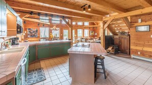 A spacious kitchen with a large island, green cabinets, and a tiled floor. - Custom Log Home-Pet-Friendly-Rio Grande River Access-Breathtaking Views (Creede)