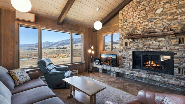 A cozy living room with a stone fireplace, leather sofas, and large windows offering a view of the mountains. - Spacious Retro Mountain Getway - ATV Parking - Amazing Views (Creede)