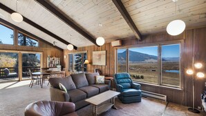 A spacious living room with a large window offering a scenic view of mountains and a lake. - Spacious Retro Mountain Getway - ATV Parking - Amazing Views (Creede)