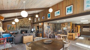 A spacious living area with a stone fireplace, wooden beams, and a dining table surrounded by chairs. - Spacious Retro Mountain Getway - ATV Parking - Amazing Views (Creede)