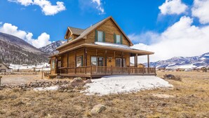 A wooden cabin with a porch, surrounded by a snowy landscape and mountains. - Cozy Home-Spectacular Mountain Views / ATVs Welcome (Creede)
