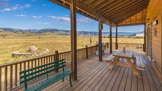 A wooden deck with a bench and picnic table, overlooking a grassy field and distant mountains. - Cozy Home-Spectacular Mountain Views / ATVs Welcome (Creede)