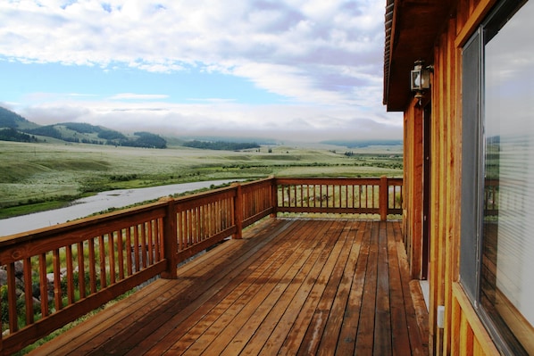 A wooden deck with a view of a river and hills.