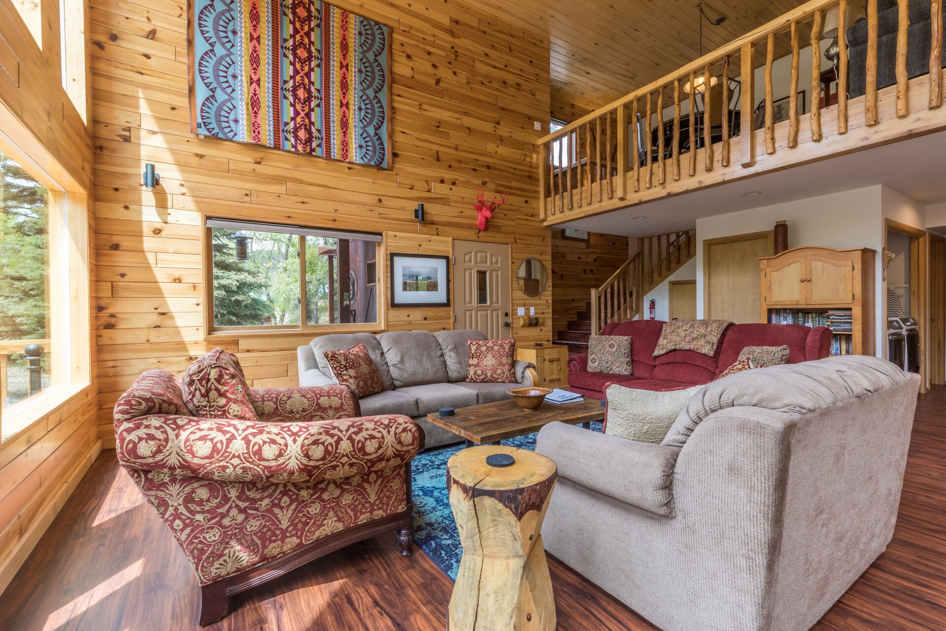 L’intérieur d’une cabane en rondins, avec un salon, un escalier et une vue sur l’extérieur.