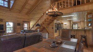 En rummelig stue med en stor lædersofa, et spisebord med servietter, en trappe, et køkkenområde og en bar.