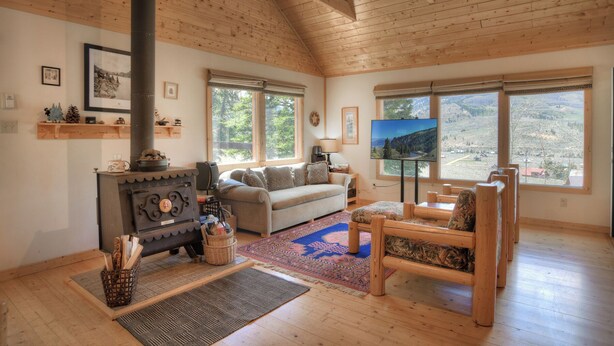 A cozy living room with a fireplace, a sofa, a TV, and large windows offering a scenic view. - Secluded Mountain Cabin - Pet Friendly - National Forest Access (Creede)