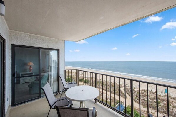 Enjoy the ocean view from this balcony with a table and chairs.